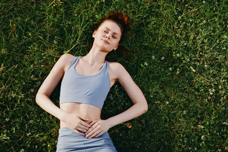 Young woman relaxing on grass in athletic wear, embodying freedom and joy, surrounded by nature in a serene setting with vibrant green colors
