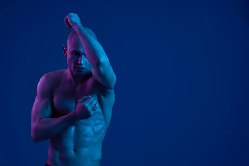 Athletic man posing against a vibrant blue background, showcasing strength and confidence through dynamic body language and dramatic lighting.