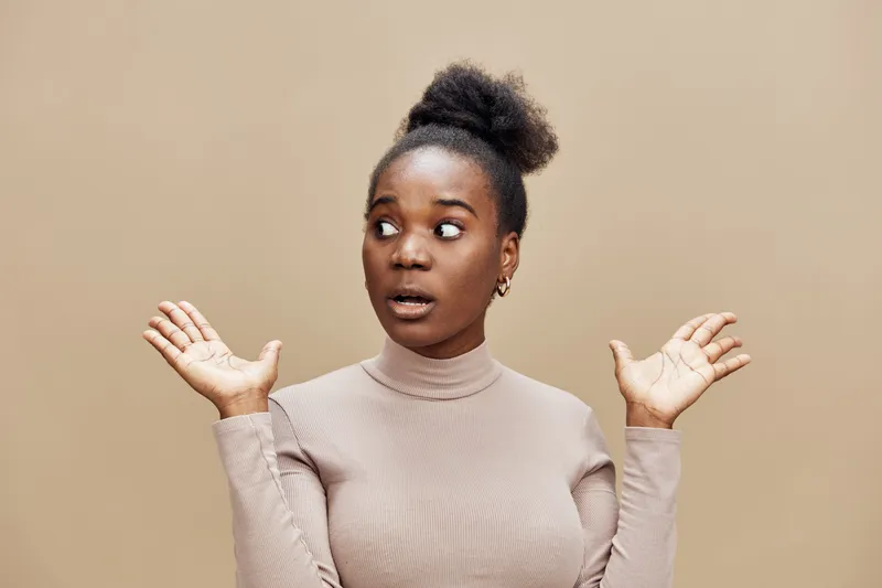 Surprised young woman in neutral toned outfit expressing disbelief against a beige background, showcasing emotions of shock and curiosity