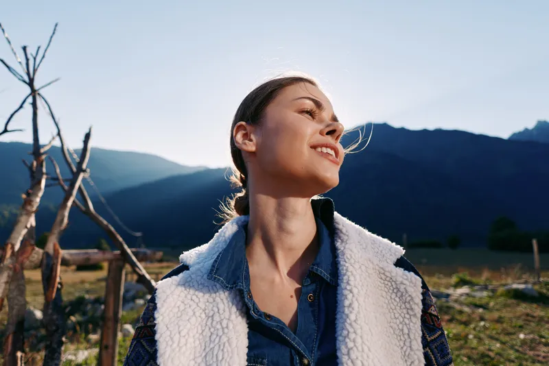 Woman smile outdoors mountains portrait nature countryside happy young woman in shearling vest and denim shirt enjoying sunlight and fresh air with a relaxed serene expression