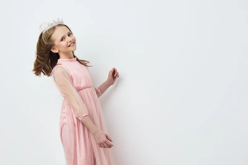 Cute girl wearing a pink dress and tiara, smiling joyfully against a neutral background, perfect for celebrations and children s events