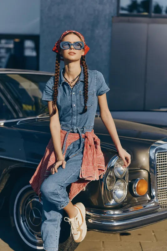 lifestyle woman in modern boho-western denim street style leans on vintage car wearing sunglasses and a patterned scarf, film color with casual confident vibe