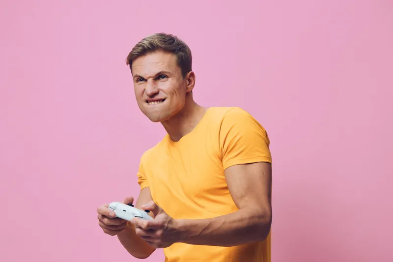 focused young man wearing yellow t-shirt playing video game holding game controller isolated on pink background digital detox gaming concept fun lifestyle