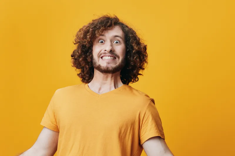 A joyful young man with curly hair wearing a yellow t shirt, expressing excitement against a vibrant yellow background, showcasing enthusiasm and positivity