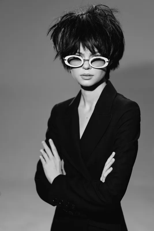 Black and white stylish woman wearing sunglasses with short hair and crossed arms posing confidently in a studio.