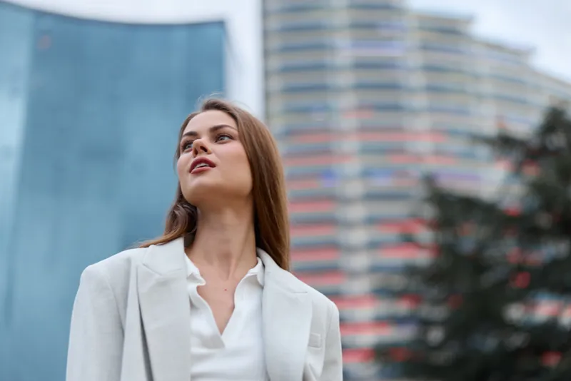 Businesswoman in a stylish outfit looking confidently at the skyline, exuding professionalism and modern elegance amidst a contemporary urban backdrop.