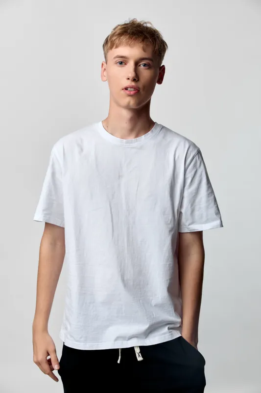 Young man casual clothing white t shirt relaxed pose studio setting fashion minimalism everyday wear male model clean background neutral palette bright lighting contemporary style wardrobe basics for