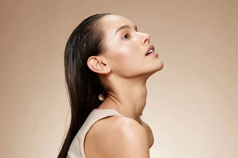 Portrait of a young woman with smooth skin and wet hair, showcasing beauty and elegance against a soft beige background, ideal for wellness and skincare concepts