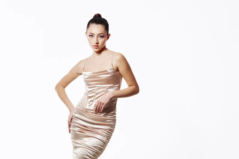 Young woman posing confidently in a silky beige dress on a white background. Creative fashion beauty concept with elegant style and modern makeup for glam look.