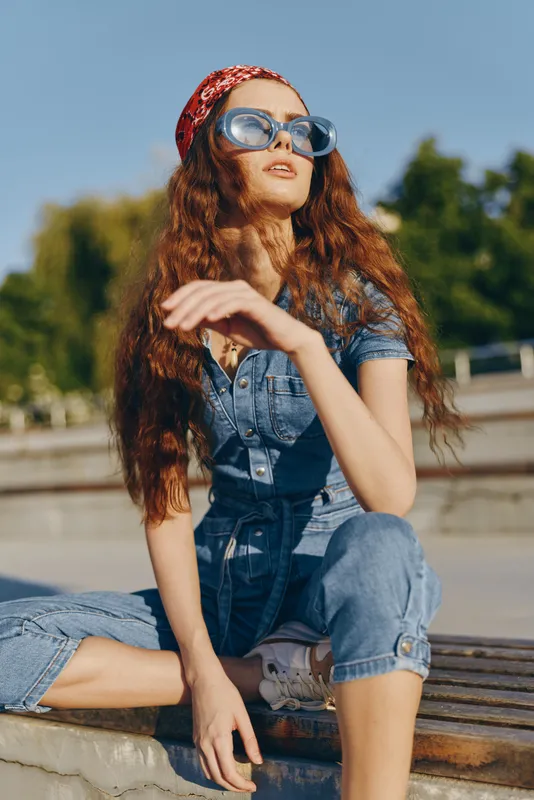 Lifestyle woman in modern boho-western denim street style with retro sunglasses and red headband, captured in warm film color tones on a sunny day outdoors.