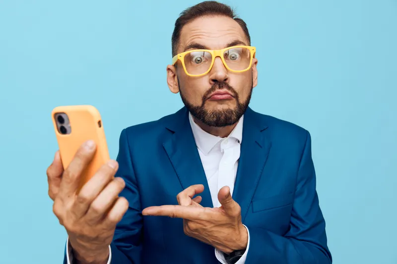 A professional man in a blue suit on a solid blue background, isolated scene with a phone in hand, expressing surprise and curiosity, suitable for business and corporate themes.