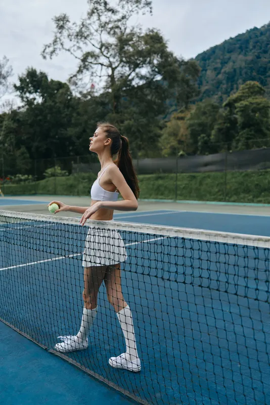 Young female tennis player practicing on a sunny court, wearing a sports bra, skirt, and knee high socks, exuding determination and focus