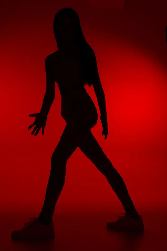 Silhouette of woman sport fitness exercising against red background, emphasizing active lifestyle, strength, and movement in dynamic pose.