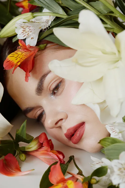 Serene beauty portrait of a young woman surrounded by vibrant flowers, showcasing natural elegance and peacefulness in a soft color palette