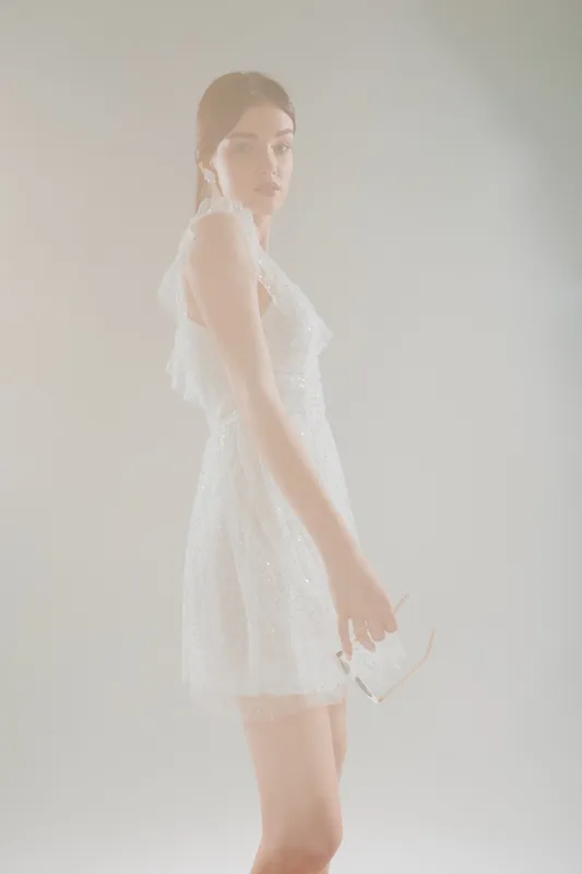Young woman in a white lace dress poses softly while holding sunglasses. Studio shot with soft lighting and a neutral background. Concept of woman beauty fashion and elegance.