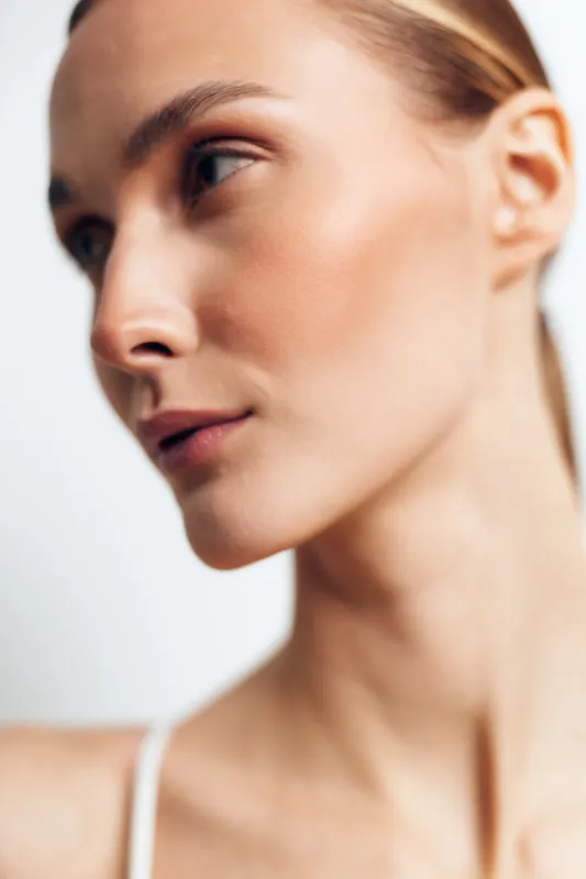 Close-up portrait of a young woman with blonde hair and clear skin looking thoughtfully to the side against a soft white background.