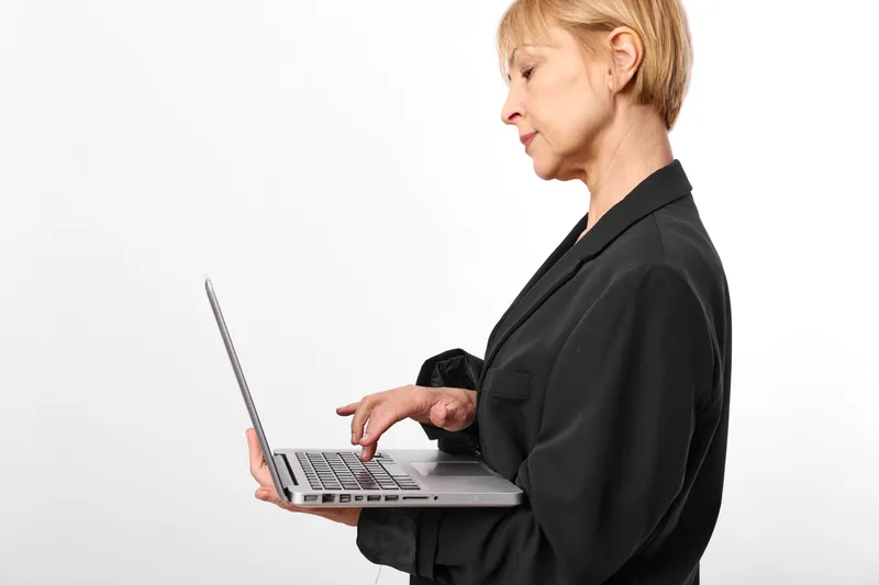 Woman with laptop in a business office, technology typing gesture, focused profile view, black outfit against white background, modern communication concept, professional atmosphere