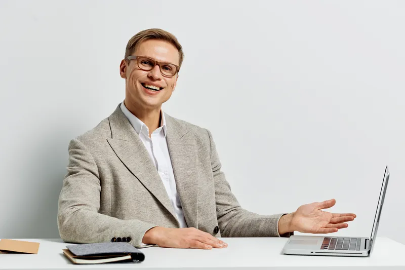 Smiling man working laptop remote digital nomad casual jacket glasses sitting white background studio portrait freelance concept