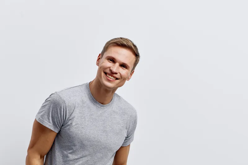 Smiling man in casual gray t-shirt looking at camera, cheerful expression, optimistic mood, clean background, studio portrait, lifestyle concept, positive vibe, young adult male.