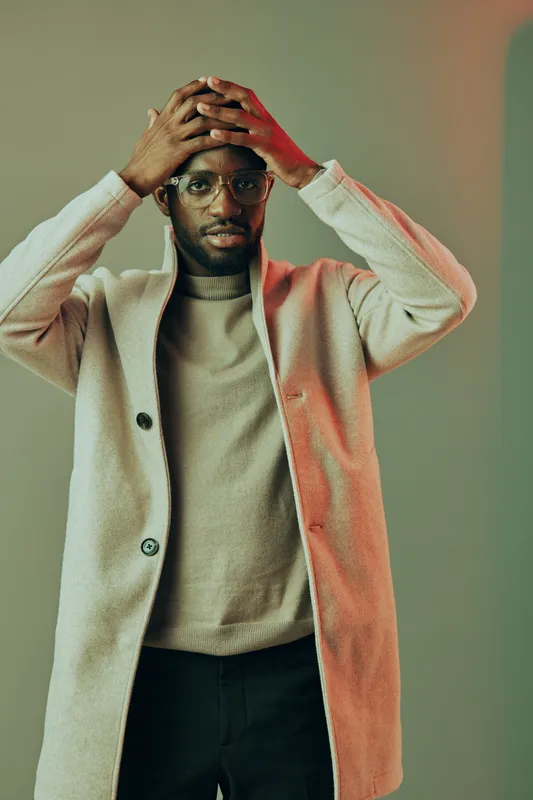 Stylish young man with glasses wearing a light coat, expressing surprise against a colorful background, reflecting modern fashion and urban lifestyle
