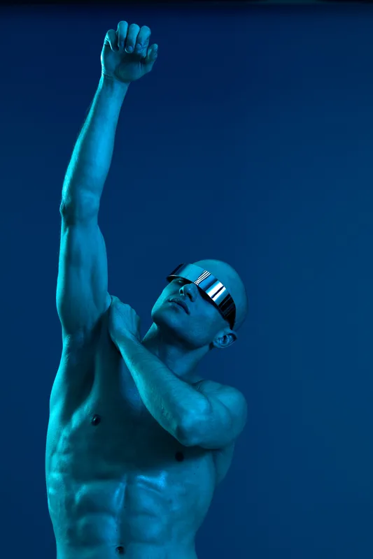 Stylish man posing confidently with a raised arm, showcasing a modern look with sunglasses. The image exhibits vibrant blue tones and a powerful aesthetic.