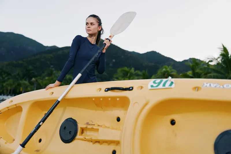Athletic figure stands on a bright yellow kayak, grasping a paddle as mountains rise in the background, capturing motion, determination, and outdoor water sport energy.