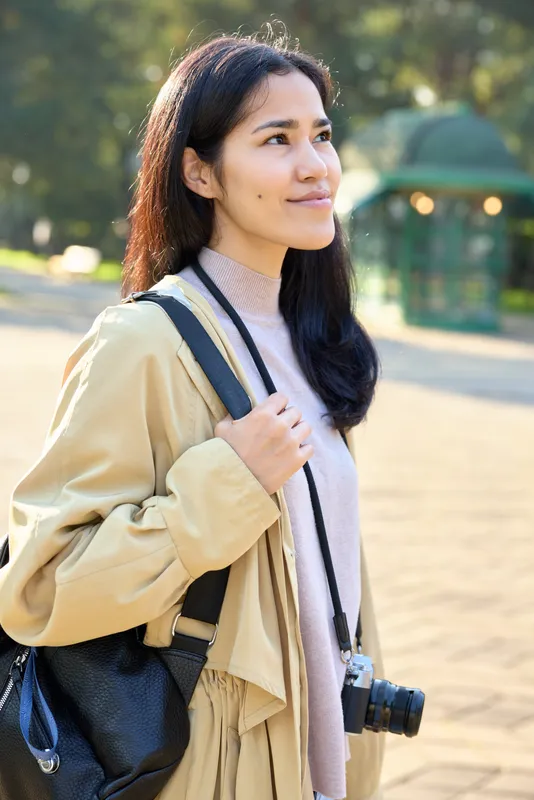 woman camera backpack outdoors park sunlight travel fashion casual relaxed exploring sunny park with camera ready moments in nature during outdoor stroll and serene mood in daylight