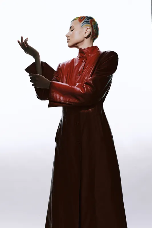 Stylish woman with colorful hair in a red leather coat posing elegantly against a white background, showcasing fashion, confidence, and modern style.