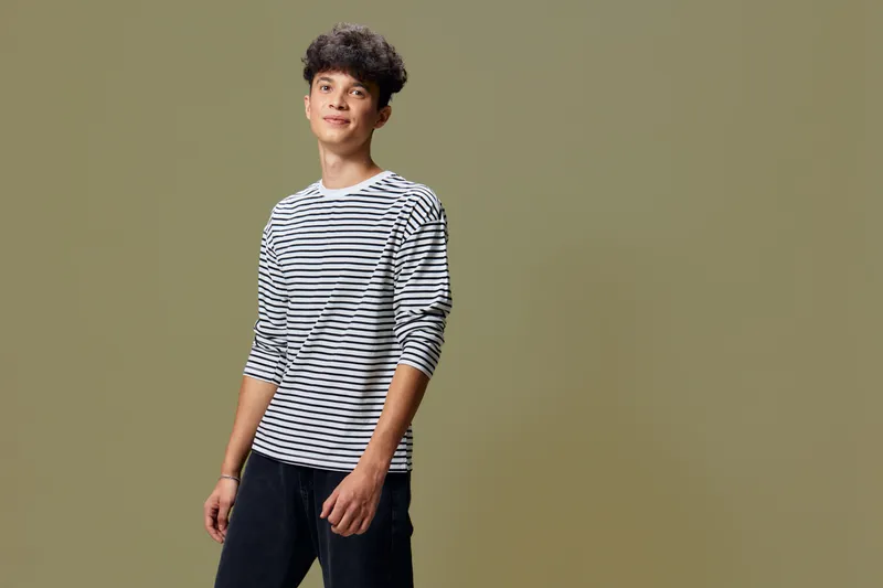 young man in striped shirt posing confidently with a neutral olive background, casual style, relaxed expression, studio portrait lighting