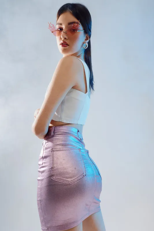 Young woman in stylish pink skirt and white top poses confidently wearing trendy sunglasses. Studio shot with soft lighting on neutral background. Concept of woman beauty fashion.