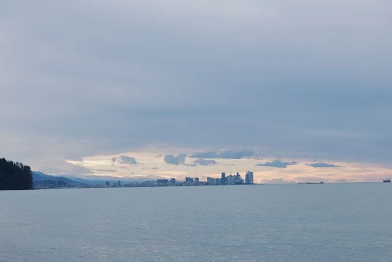 Water and distant skyline over a calm lake at dusk, cloudy sky and tranquil horizon, wide landscape with silhouettes across the water, serene evening scene for travel, nature, and cityscape projects.