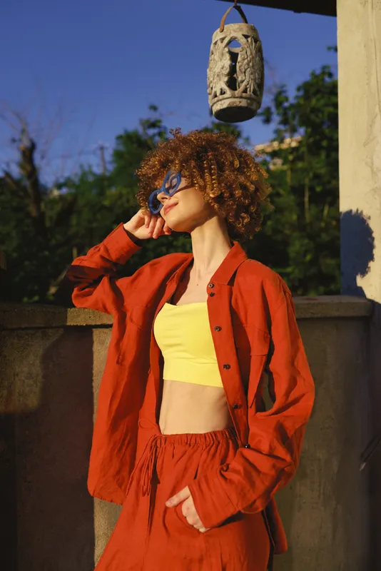Vibrant woman outdoors in a sunny moment, wearing a yellow crop top with a red jacket, stylish pose, relaxed confidence, warm tones and natural shadows, lifestyle, photogenic moment, moment, candid