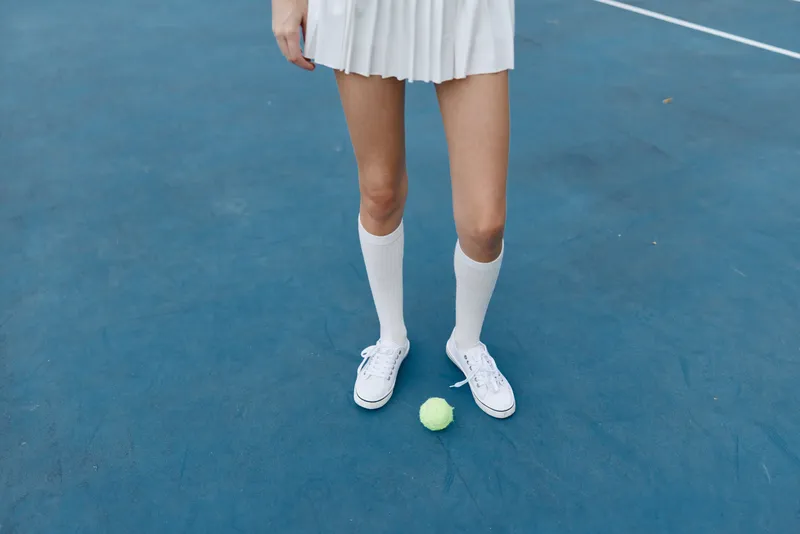 Young female athlete in a tennis outfit standing on a blue court with a tennis ball, showcasing athleticism and sportiness during a sunny day