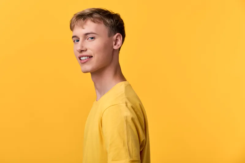 Young man in a yellow shirt stands against a bright yellow backdrop, delivering a cheerful casual vibe ideal for lifestyle, fashion and promotional campaigns with clean composition and adaptable tone
