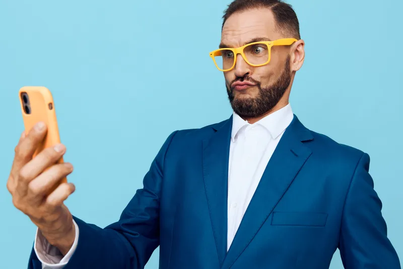 Professional man in a blue suit strikes a confident pose with a focused, friendly expression against an isolated solid blue background. This shot conveys business professionalism and emotional