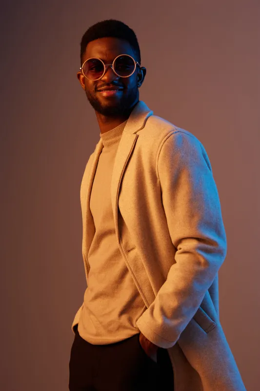 Stylish young Black man in modern clothing with oversized sunglasses, looking confidently at the camera against a gradient background
