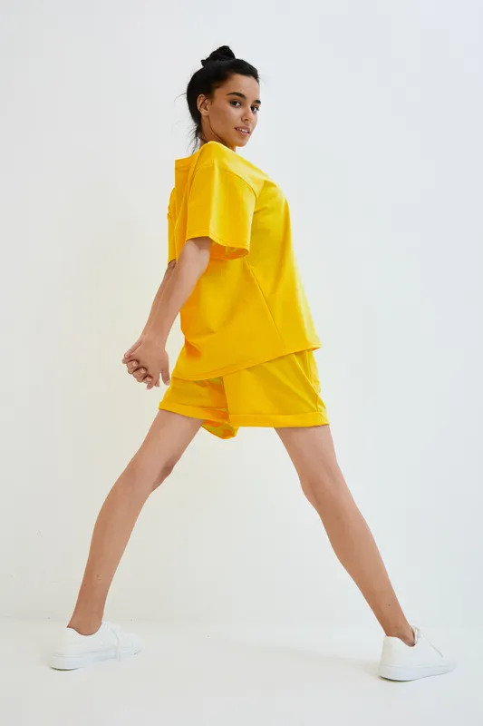 Young woman in bright yellow casual outfit posing dynamically against white background, showcasing sporty style and youthful energy in modern fashion.