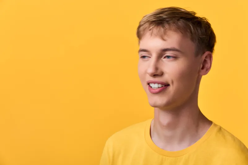 Young man with a bright smile wearing a yellow shirt stands against a vivid yellow backdrop, radiating cheerful energy, casual style, and optimistic mood for lifestyle, fashion, or marketing imagery