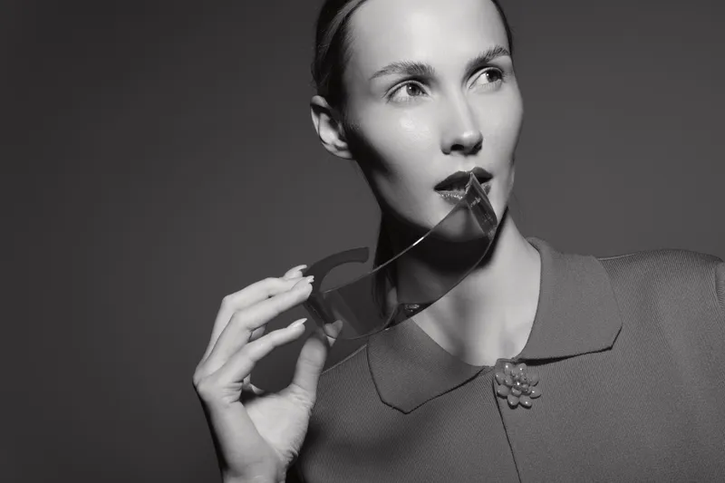 Portrait of a fair skinned white woman with slicked back hair holding sunglasses near lips. Studio fashion concept with dramatic lighting and stylish vintage clothing.