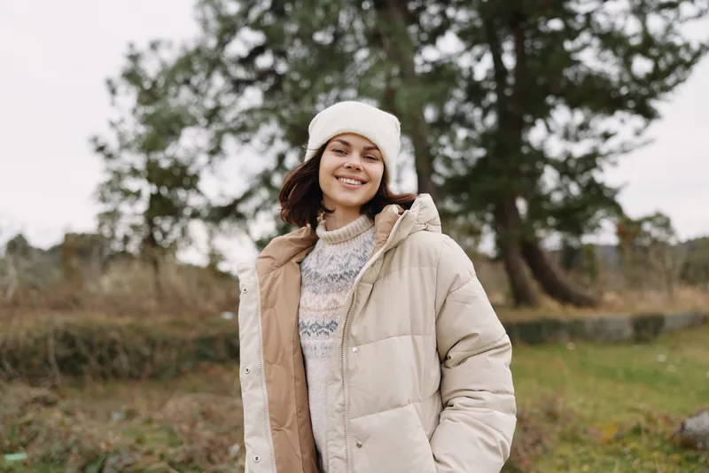 woman outdoor winter coat smiling beanie in a spacious natural park setting, enjoying a crisp day, casual fashion and everyday comfort in a peaceful outdoor scene