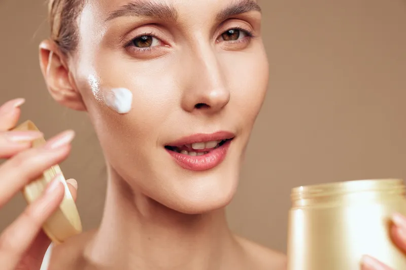 A woman applies cream to her cheek, highlighting a skincare routine and healthy glow in a bright setting. Close up of self care, moisture, and beauty with a calm mood.