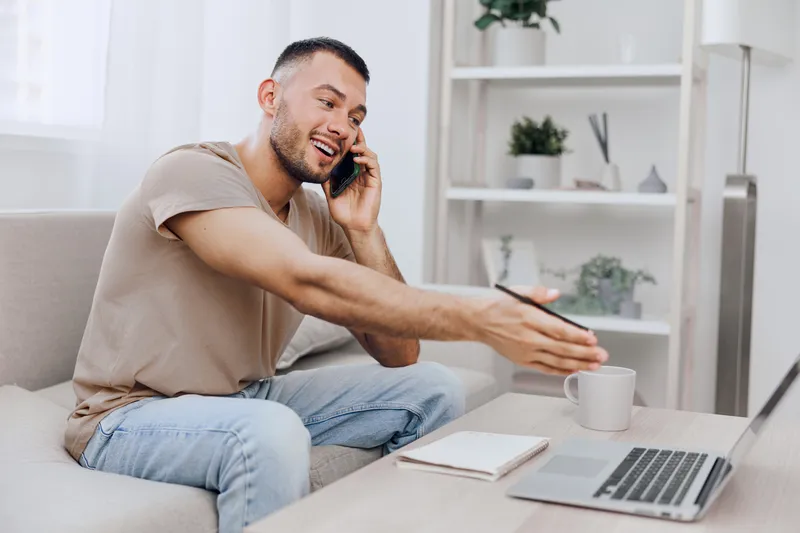 Happy man communicating on the phone while working from home, showcasing modern lifestyle and remote work trends. Capturing the essence of productivity and connection.