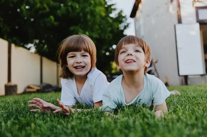 Two joyful children playing on the grass, smiling broadly, enjoying a sunny day. A perfect moment of childhood happiness and carefree nature awaits discovery.