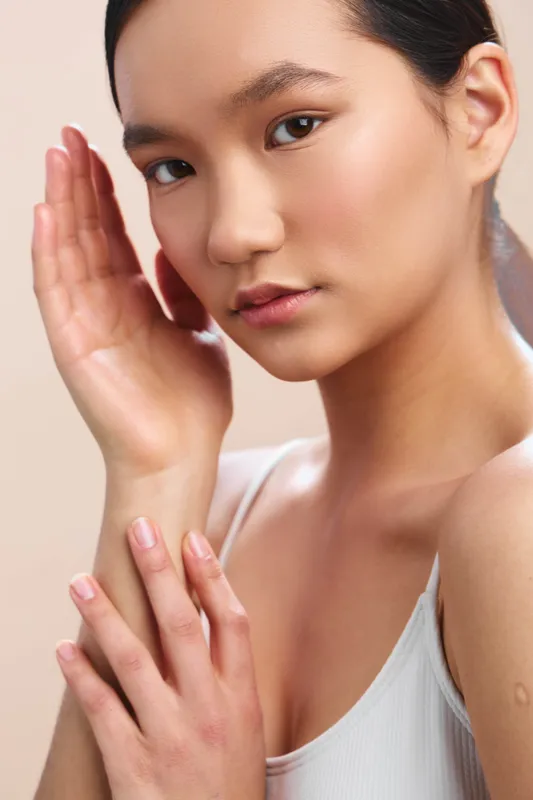 Asian woman in a close up portrait demonstrates calm skin care moment with soft lighting, clear skin, and a serene, confident expression.