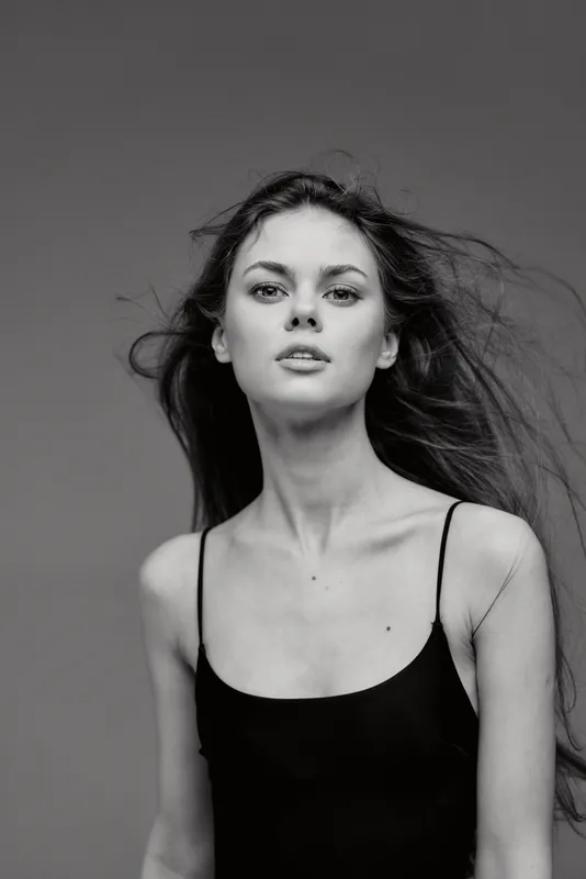 Black and white portrait of a young woman with flowing hair and a serious expression wearing a black dress.