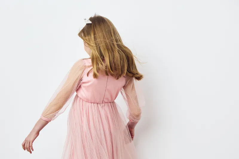 Young girl in a pink tulle dress turning away, showcasing a sense of innocence and joy in a soft and bright setting Perfect for concepts of childhood and fashion