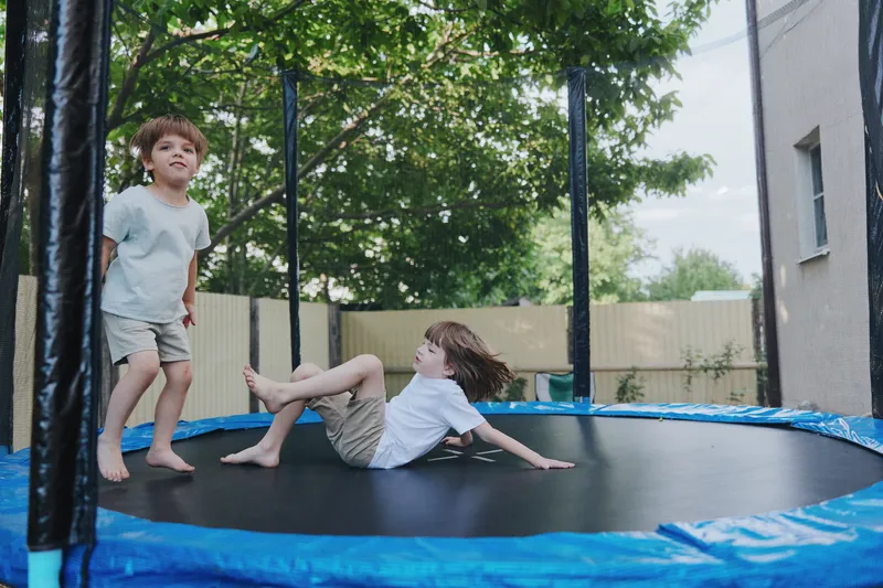 Playful boys enjoying a sunny day on a trampoline in a backyard, showcasing joy and energy while having fun outdoors with friends.