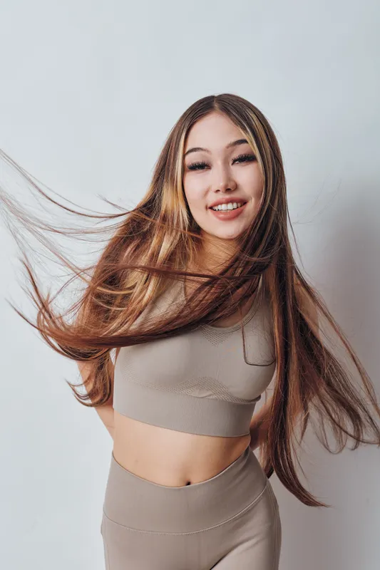 Young woman with long hair smiling and moving for dynamic portrait in casual outfit on neutral background with natural beauty and cheerful expression.