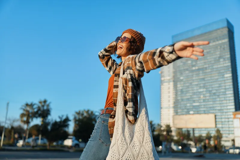 Woman joyful urban freedom fashion smile sunset candid lifestyle in city plaza, authenticity and golden hour glow, mindful living and emotional storytelling capturing a sincere moment.