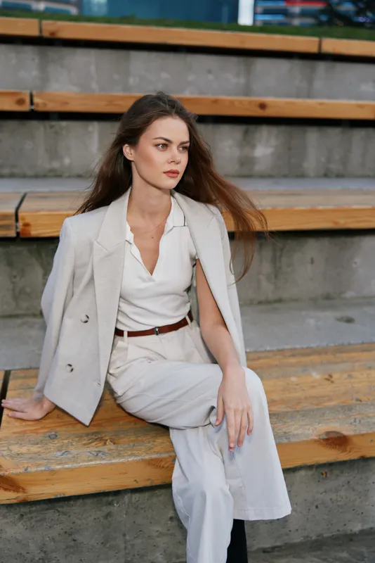 Businesswoman in elegant attire, exuding confidence and professionalism, sitting on wooden steps with a stylish background and neutral color palette.